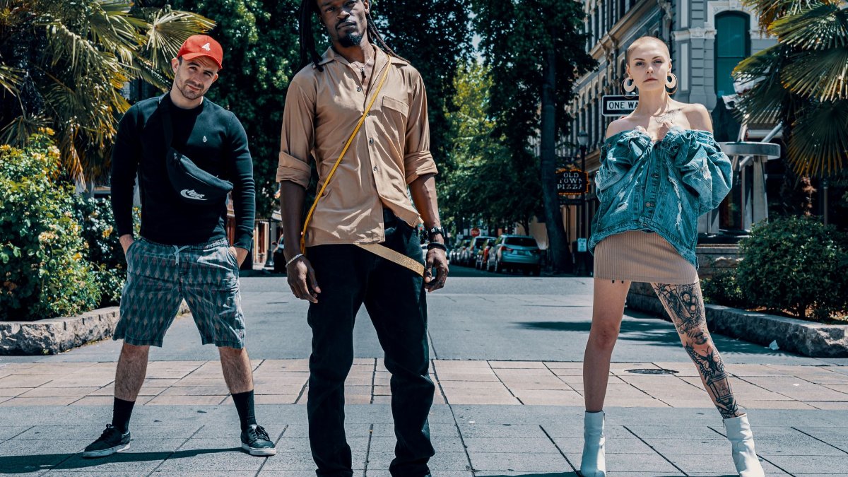 Three stylish individuals posing confidently on a sunny urban street, showcasing modern fashion trends.