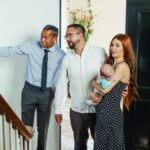 A family with a baby tours a new home with a realtor, exploring indoor spaces and possibilities.