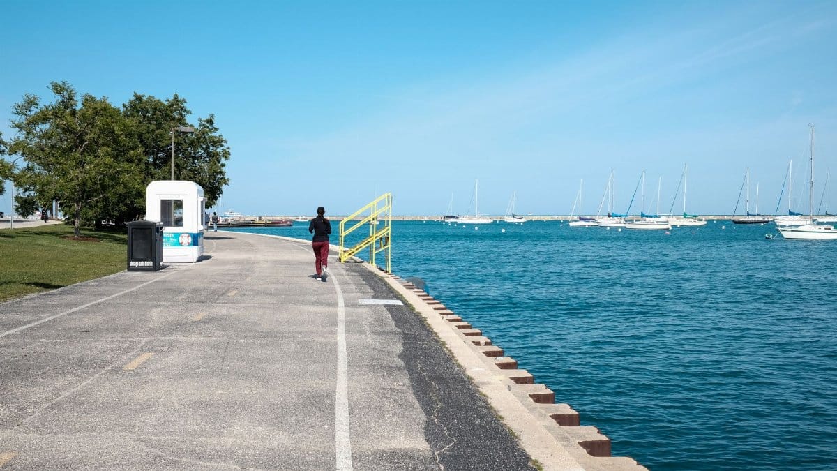 A person jogging along the scenic Chicago lakefront with boats in the background.