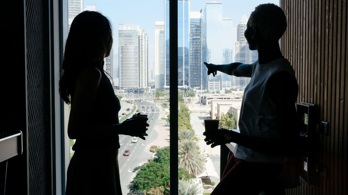 Side view of anonymous diverse business partners with coffee talking about job while admiring tall contemporary buildings of large megapolis