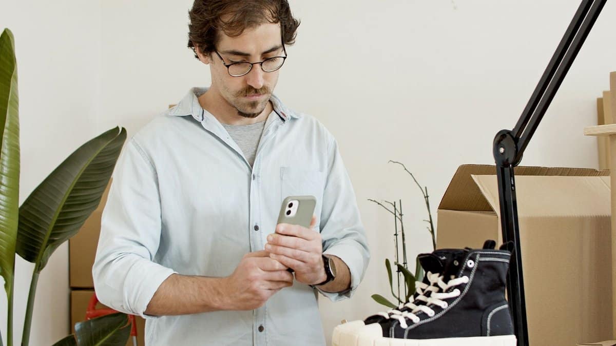 Man uses phone to photograph sneakers in an indoor business setup with boxes.