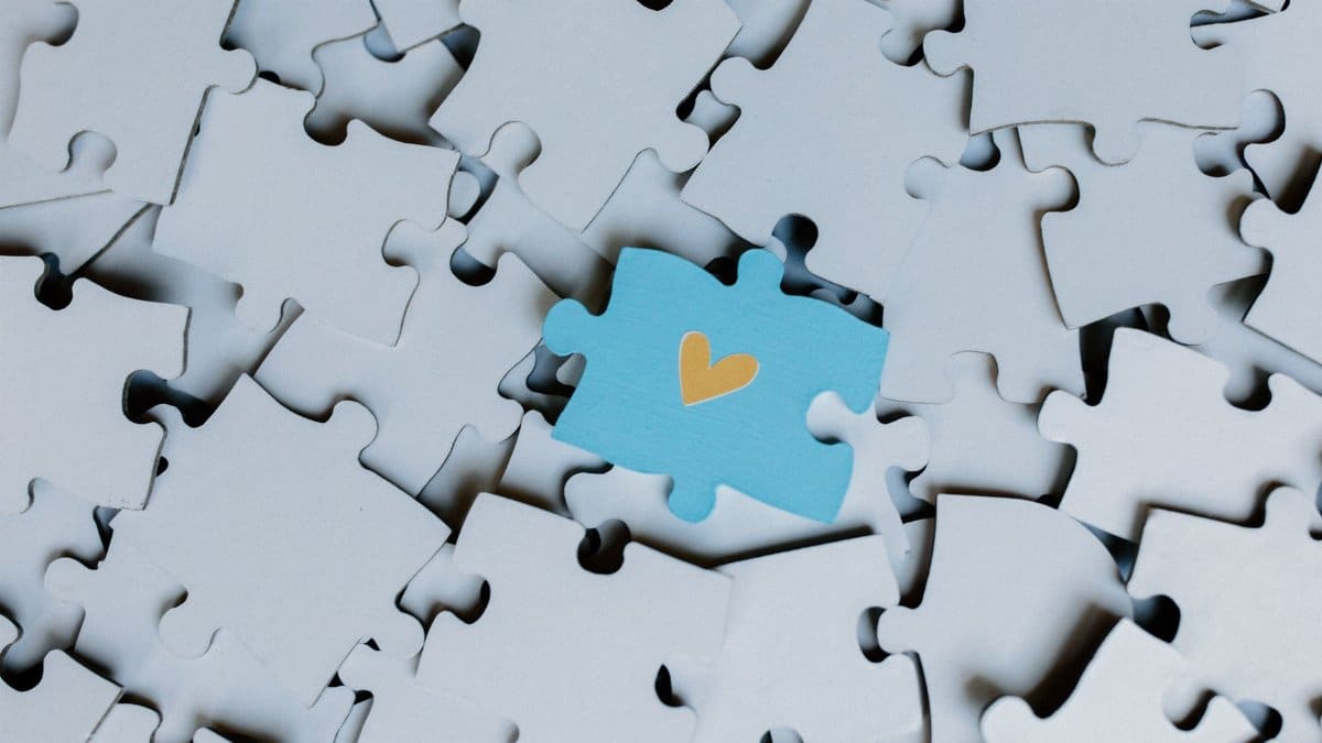 A standout blue puzzle piece with a heart symbol among white puzzle pieces, showing uniqueness.