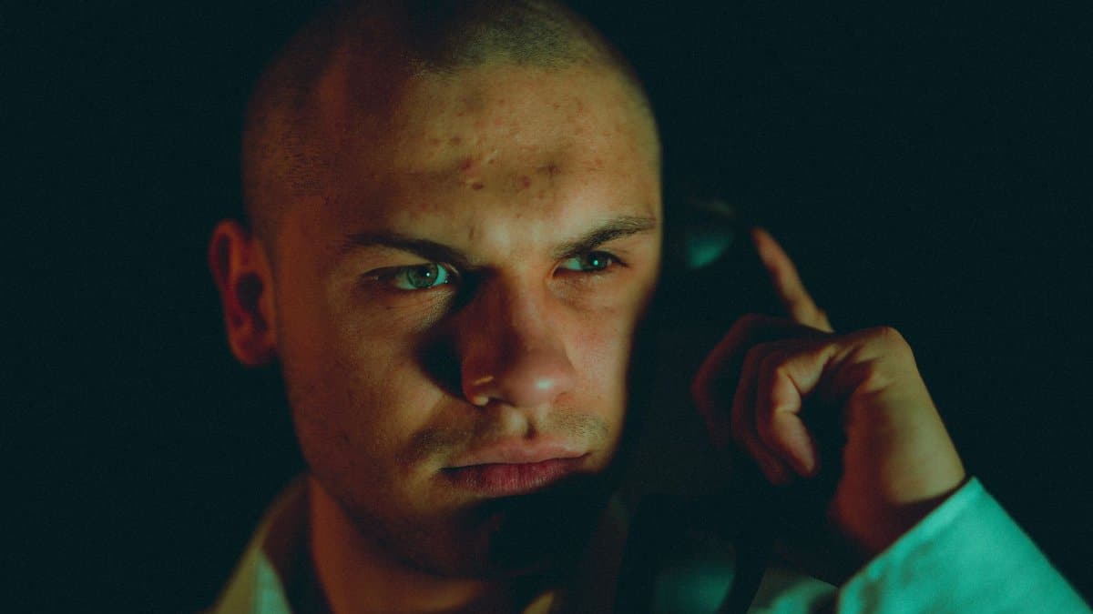 A close-up of a serious man making a phone call in dim lighting, highlighting intense facial expression.