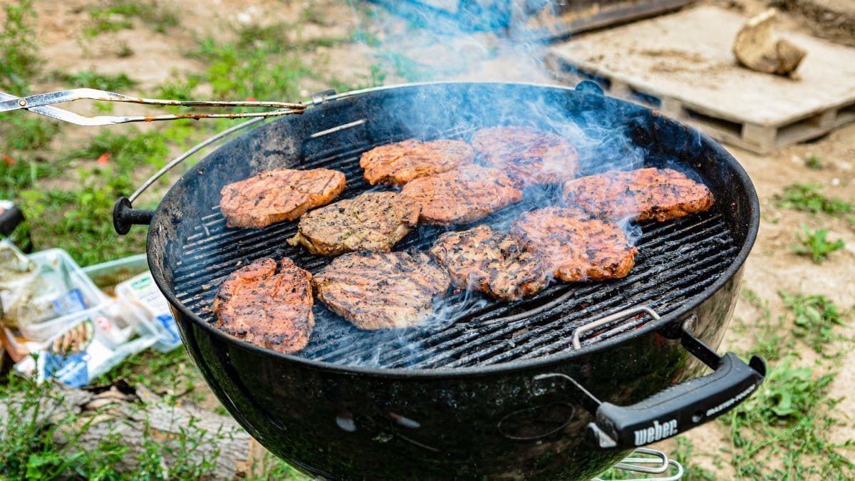 Grilled steaks sizzling on a charcoal grill with smoke, perfect for a summer barbecue.