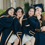 Four female graduates in gowns celebrating their achievement with joy.
