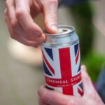 Close-up of a person opening a can of oatmeal stout beer with a Union Jack design outdoors.