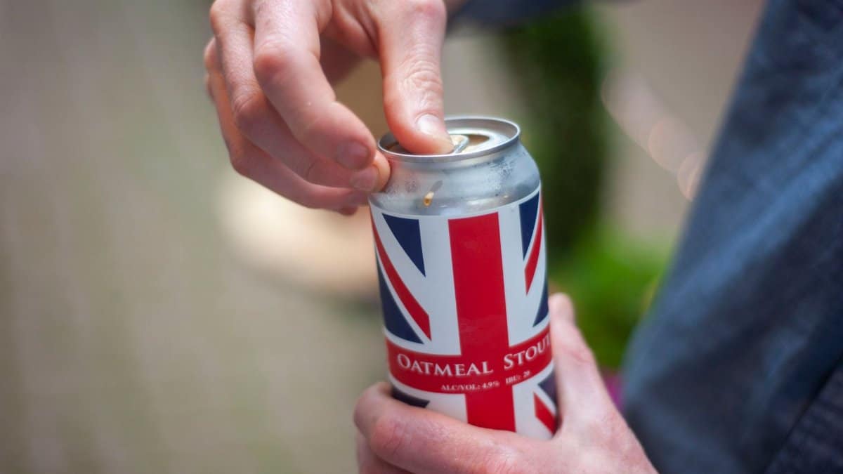 Close-up of a person opening a can of oatmeal stout beer with a Union Jack design outdoors.