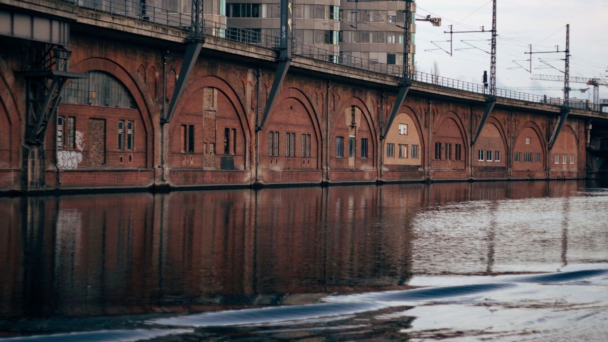 Reflection of a brick bridge and urban buildings over a canal, showcasing city architecture.
