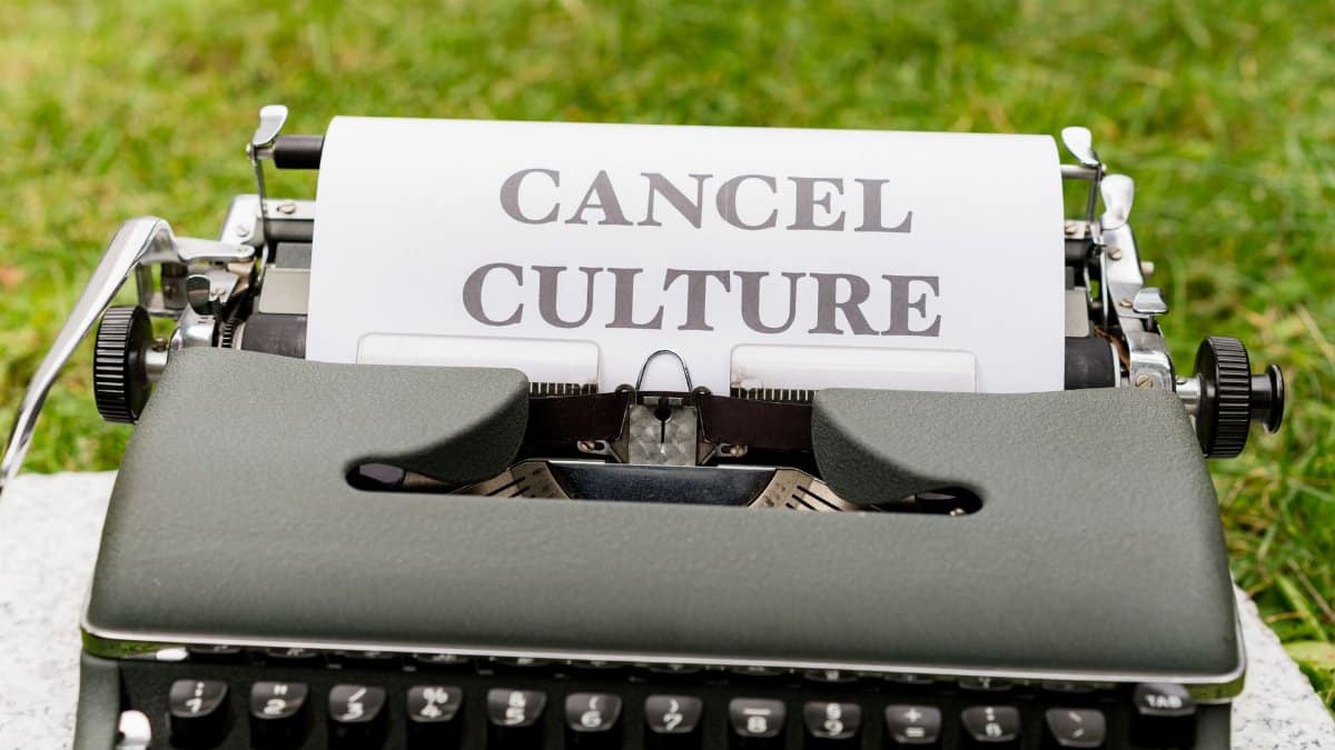 Retro typewriter with 'Cancel Culture' typed paper on grass background outdoors.