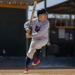 Dynamic image of a baseball player swinging at bat during a daytime game on the field.