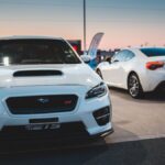 Front of sports car and rear of coupe car parked in gas station in town in evening against clear sky
