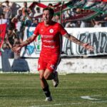 Excited soccer player celebrates scoring a goal with cheering fans in background.