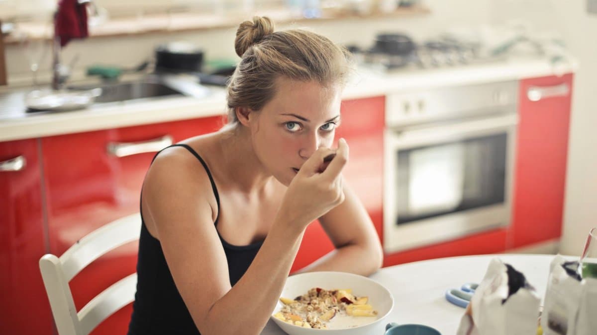 Woman eating a healthy breakfast with cereal and milk at a kitchen table.