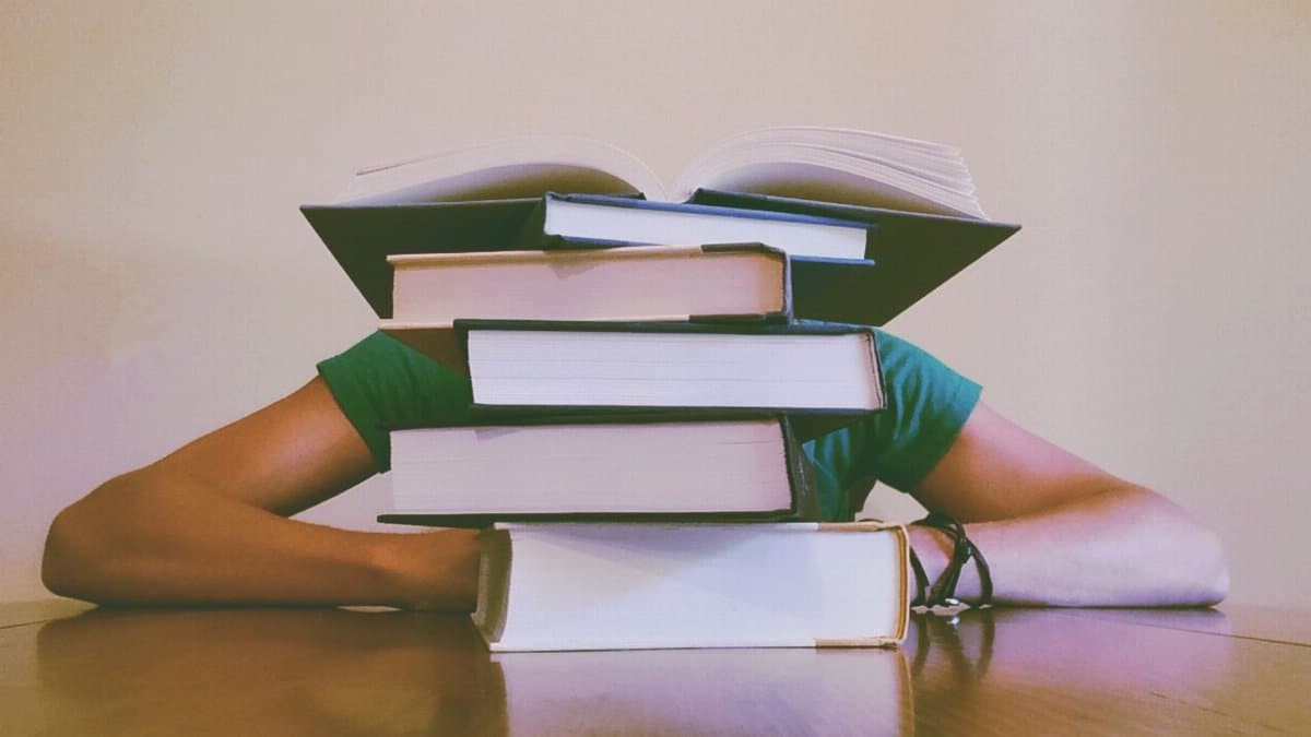 A student hidden behind a stack of books, symbolizing academic stress and study challenges.