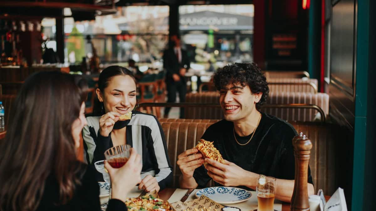 Group of friends laughing and eating at a restaurant, enjoying leisure time.