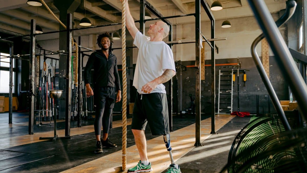 Two men engaged in adaptive fitness training with climbing ropes in a modern gym setting.