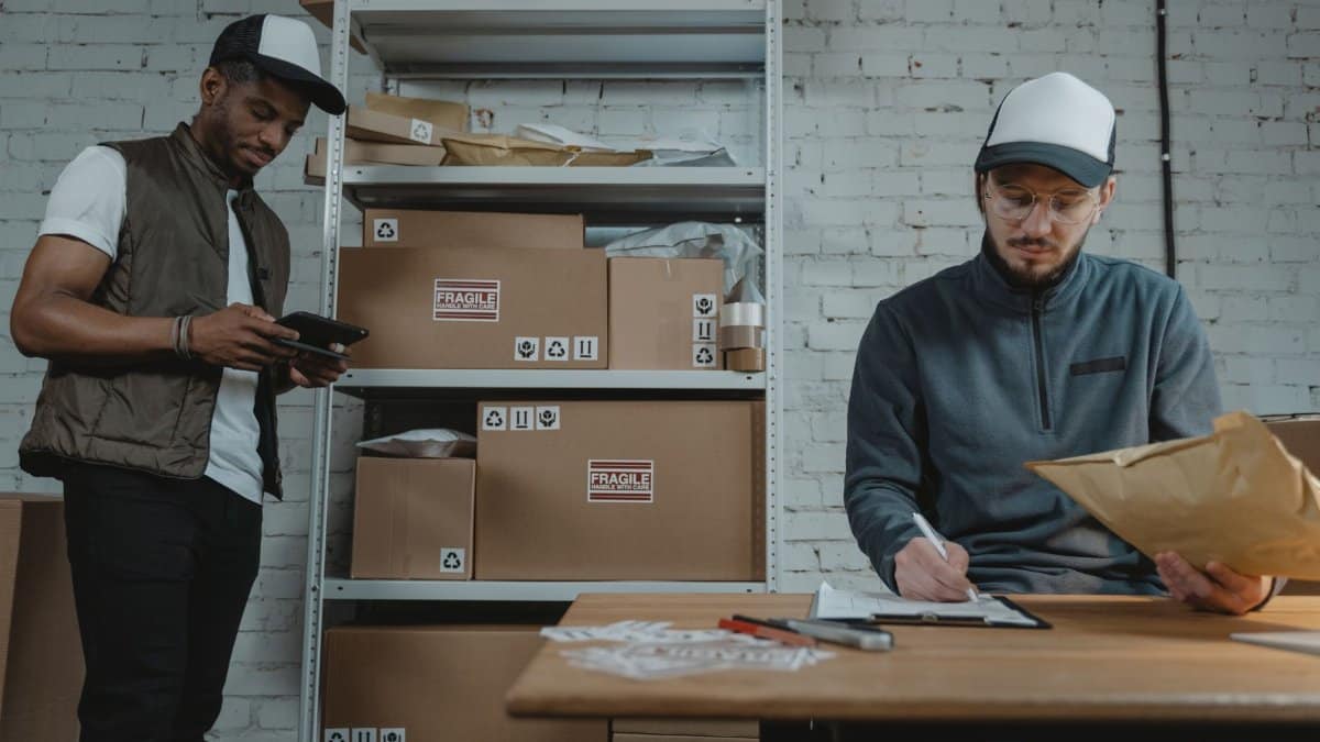 Warehouse employees organizing shipments with packages and documentation in a brick-walled workspace.
