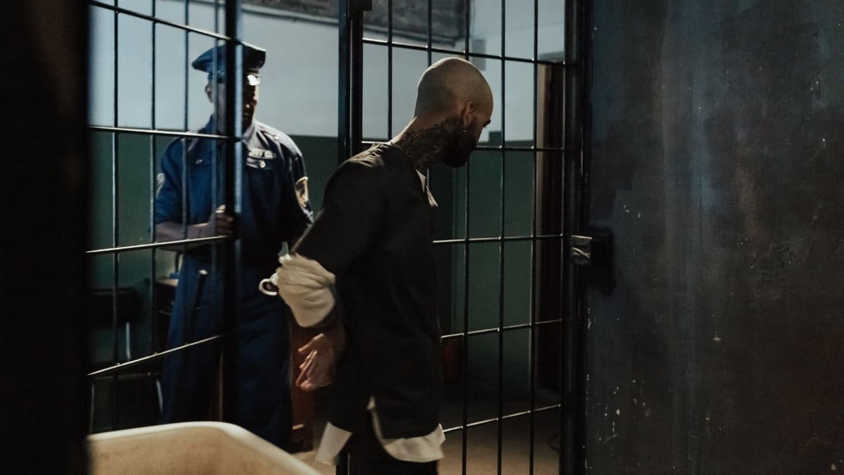 Police officer escorting a handcuffed prisoner through a dimly lit jail corridor.
