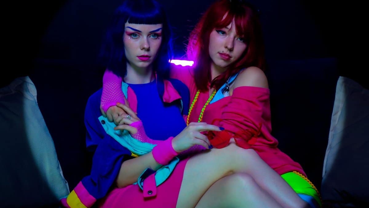 Bright neon lighting highlights two fashionable women sitting together.