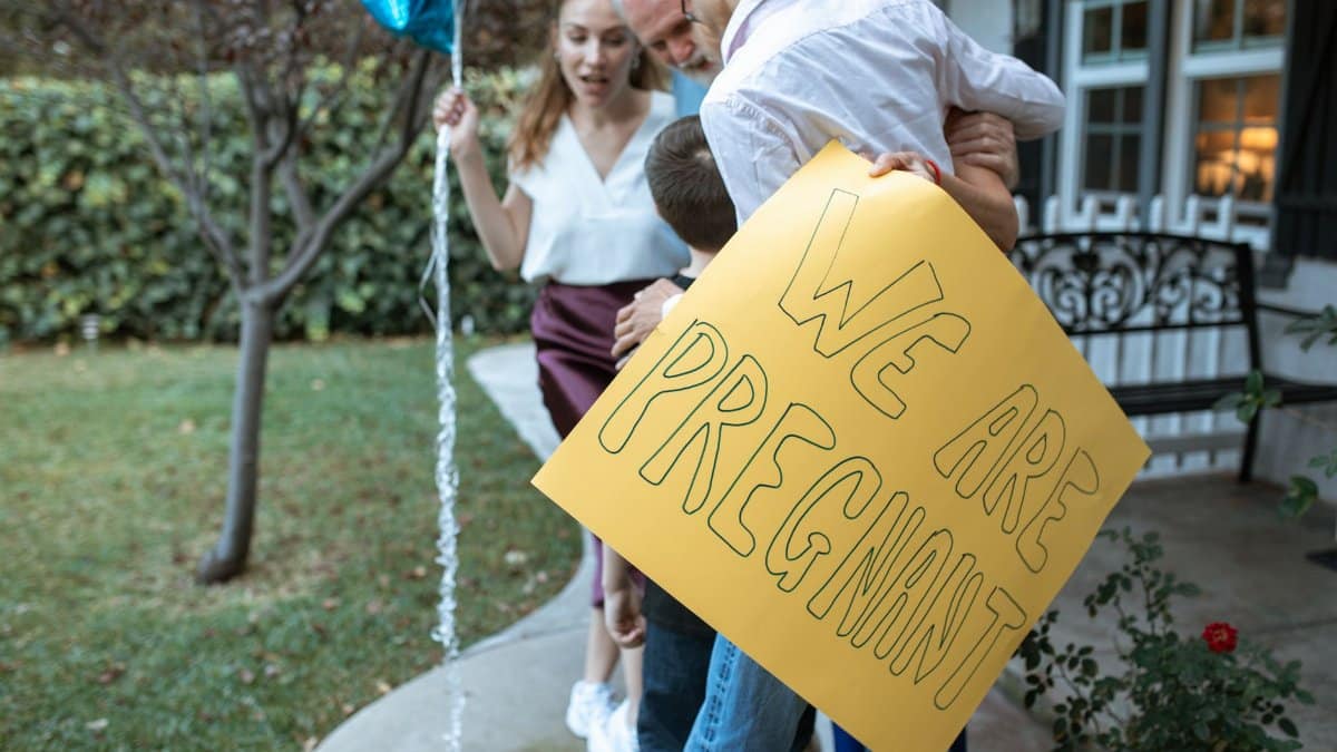 A family holding a sign announcing pregnancy, filled with joy and celebration outdoors.