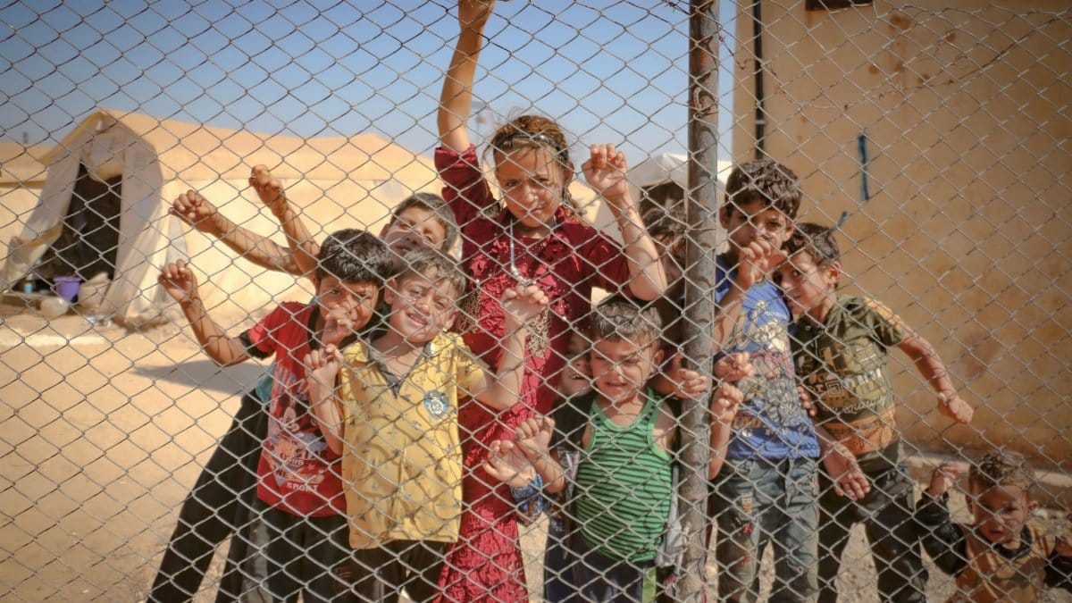 Children gather behind a fence in a refugee camp in Idlib, Syria, highlighting the challenges faced by refugees.