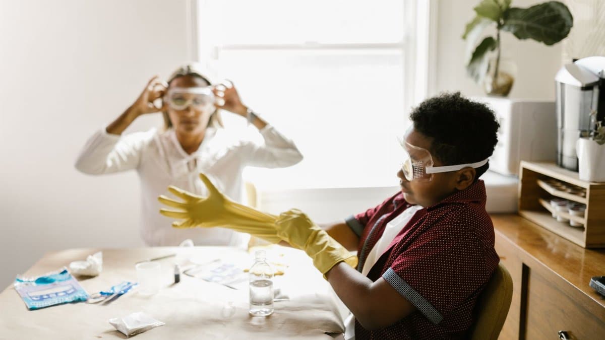 Two people engage in a science experiment wearing protective gear including goggles and gloves.