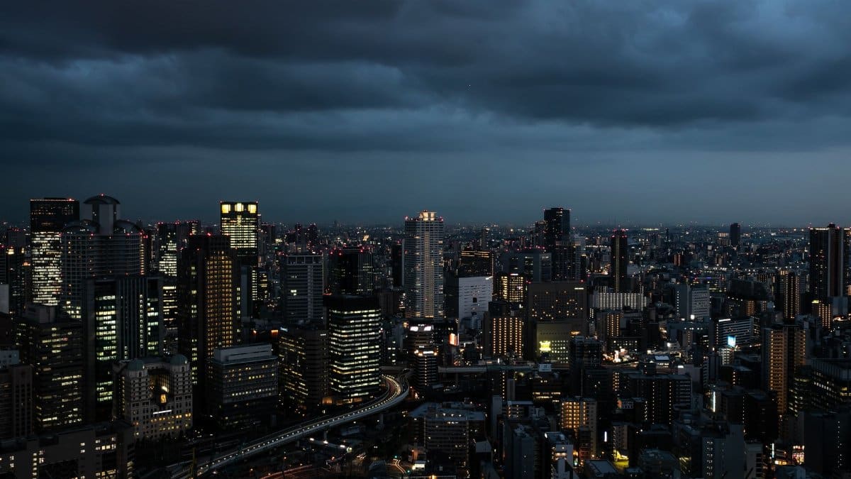 Dramatic Osaka skyline at twilight, showcasing illuminated skyscrapers against moody clouds.