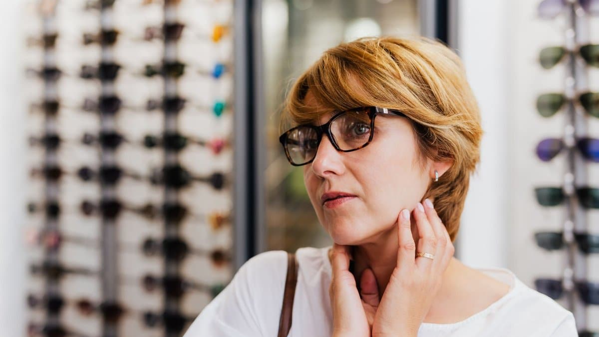 Woman examining new eyewear in store with diverse eyeglasses selection in the background.