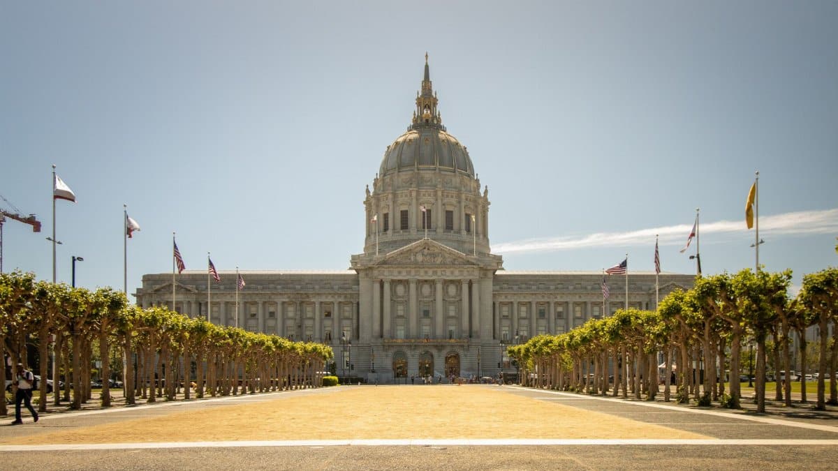 Elegantly ornate San Francisco City Hall with flags and trees lining the path.