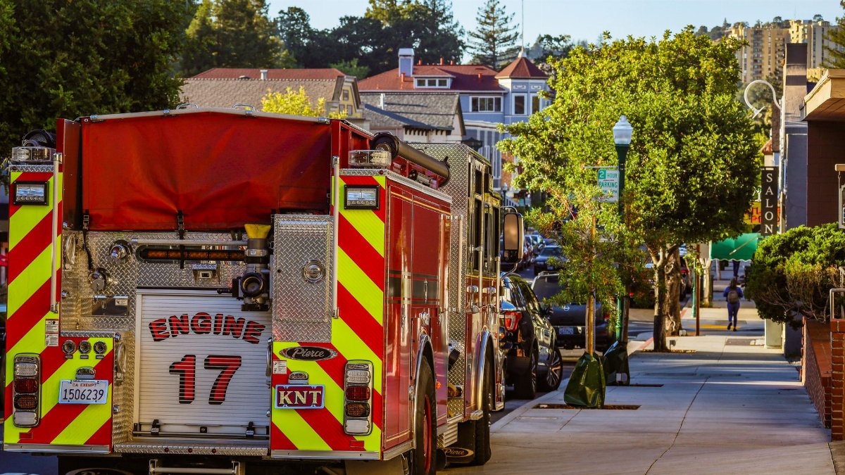 A fire engine parked on a city street with buildings and clear sky in the background.