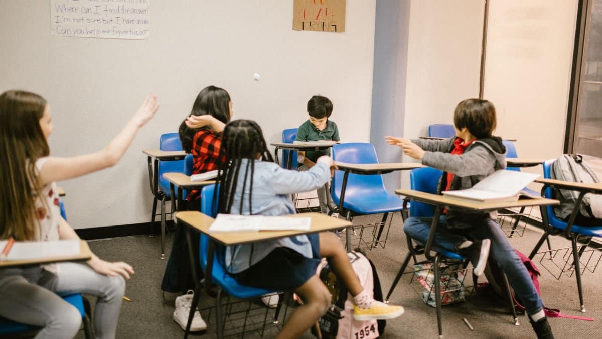 A classroom of children interacting, with one child appearing isolated.