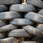Pile of black rubber tires stacked outdoors in daylight.