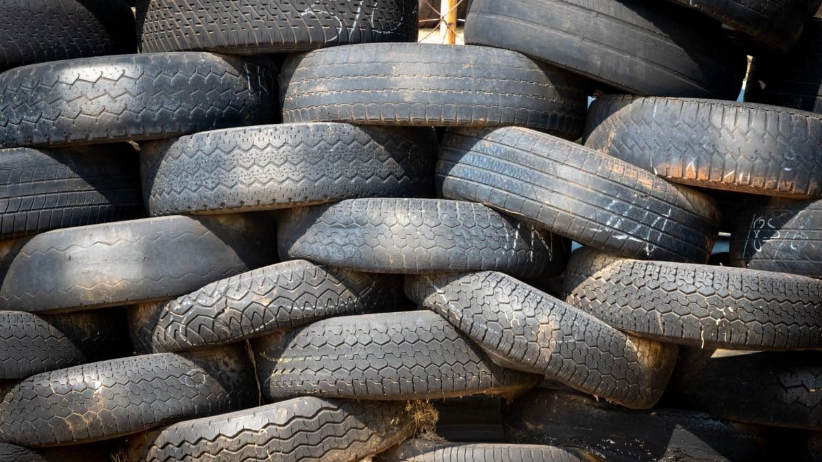 Pile of black rubber tires stacked outdoors in daylight.