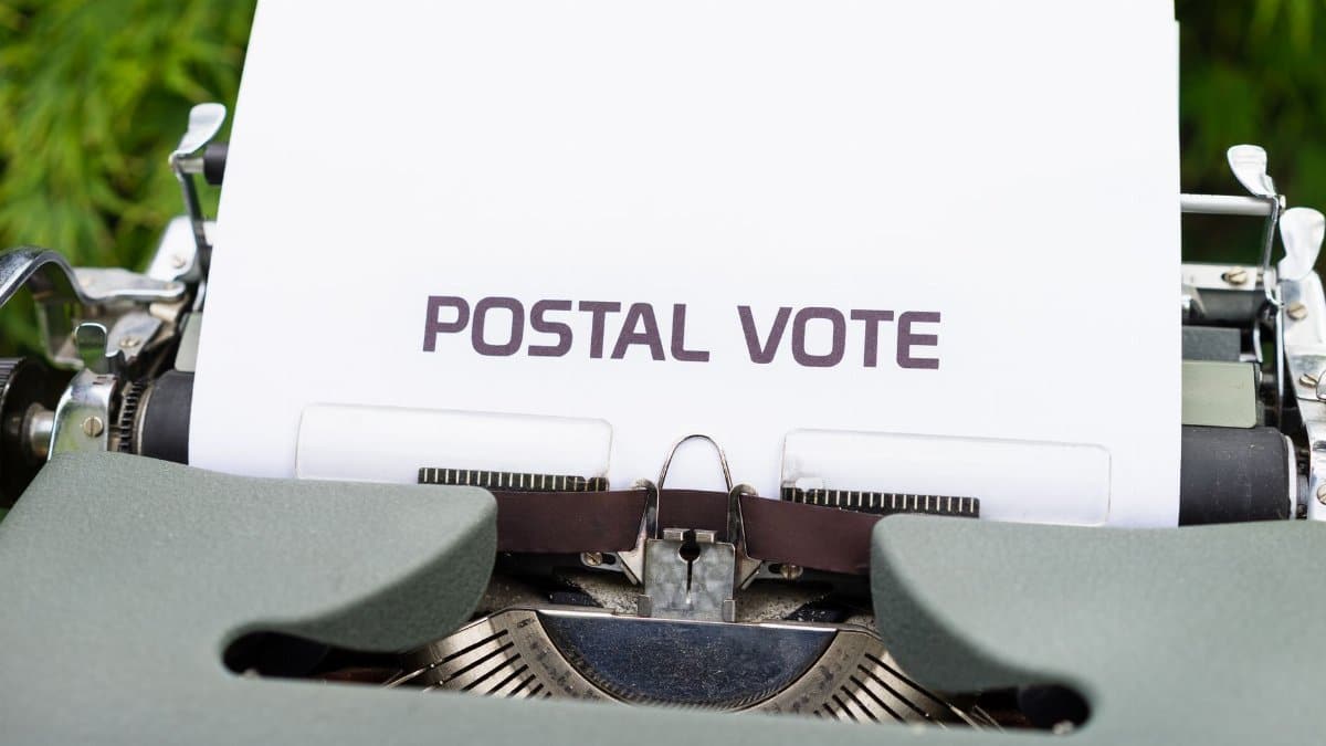 Close-up of typewriter with paper displaying the words 'Postal Vote', outdoors.