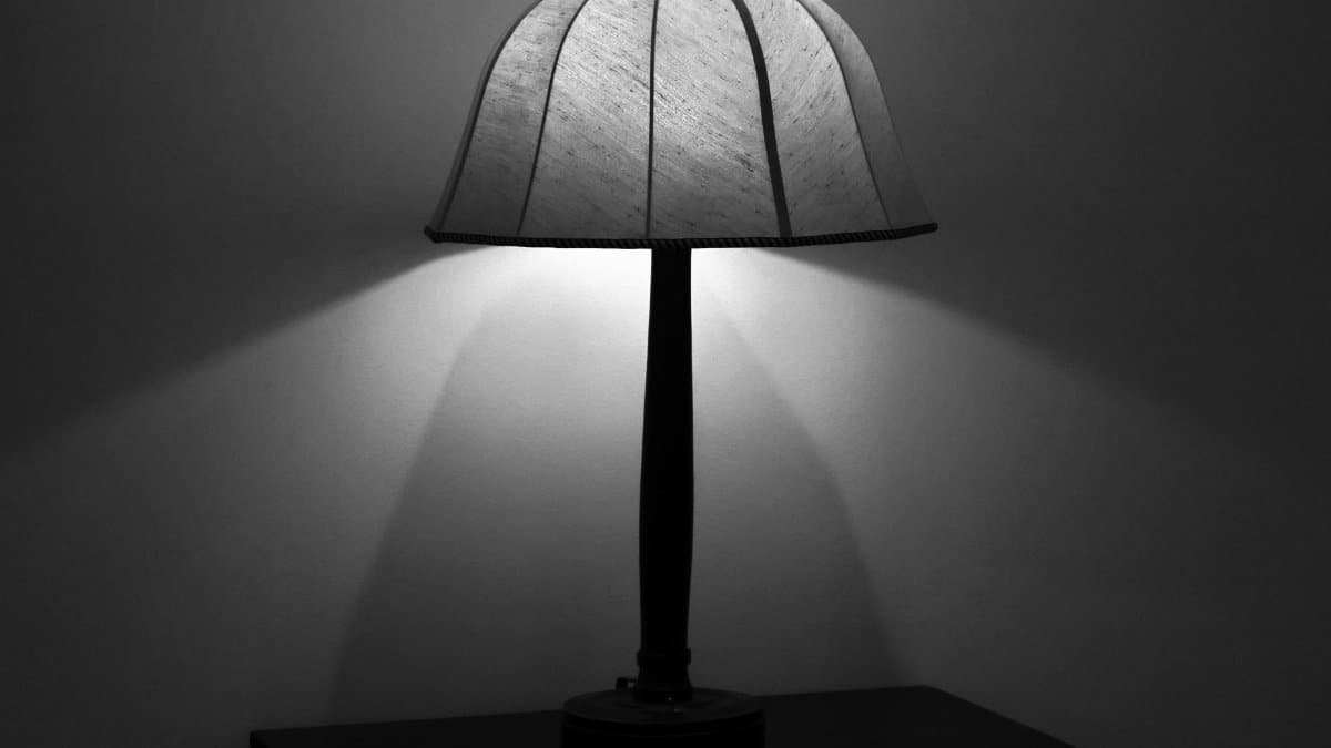 A minimalist black and white photo of a table lamp casting soft light in a dark room.