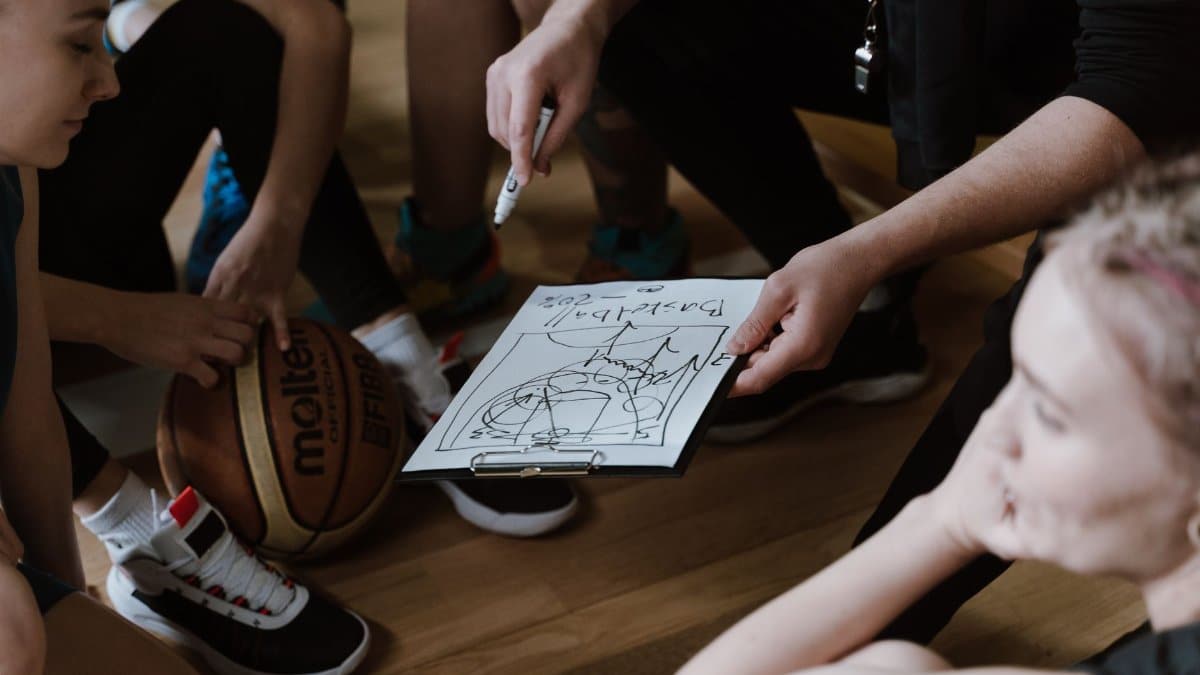 Close-up of a basketball team huddling with the coach discussing strategy indoors.