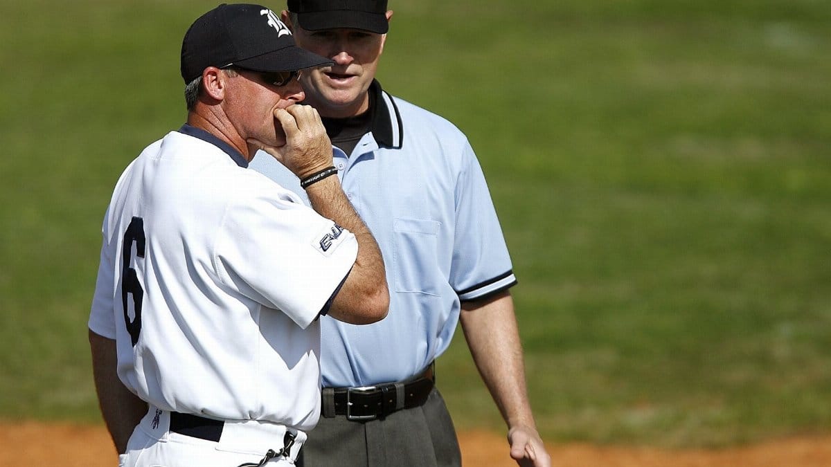 A baseball coach engages with an umpire on the field, discussing game strategy in uniform under a clear sky.