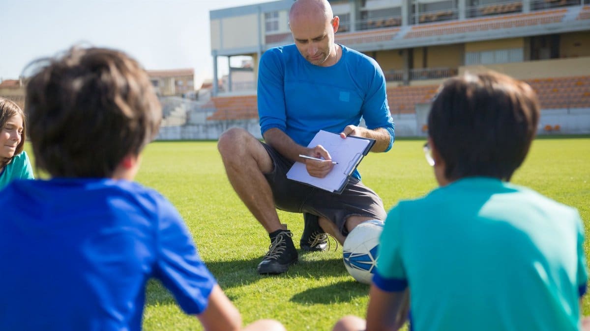 Coach inspiring young players during soccer practice at a Portuguese stadium.