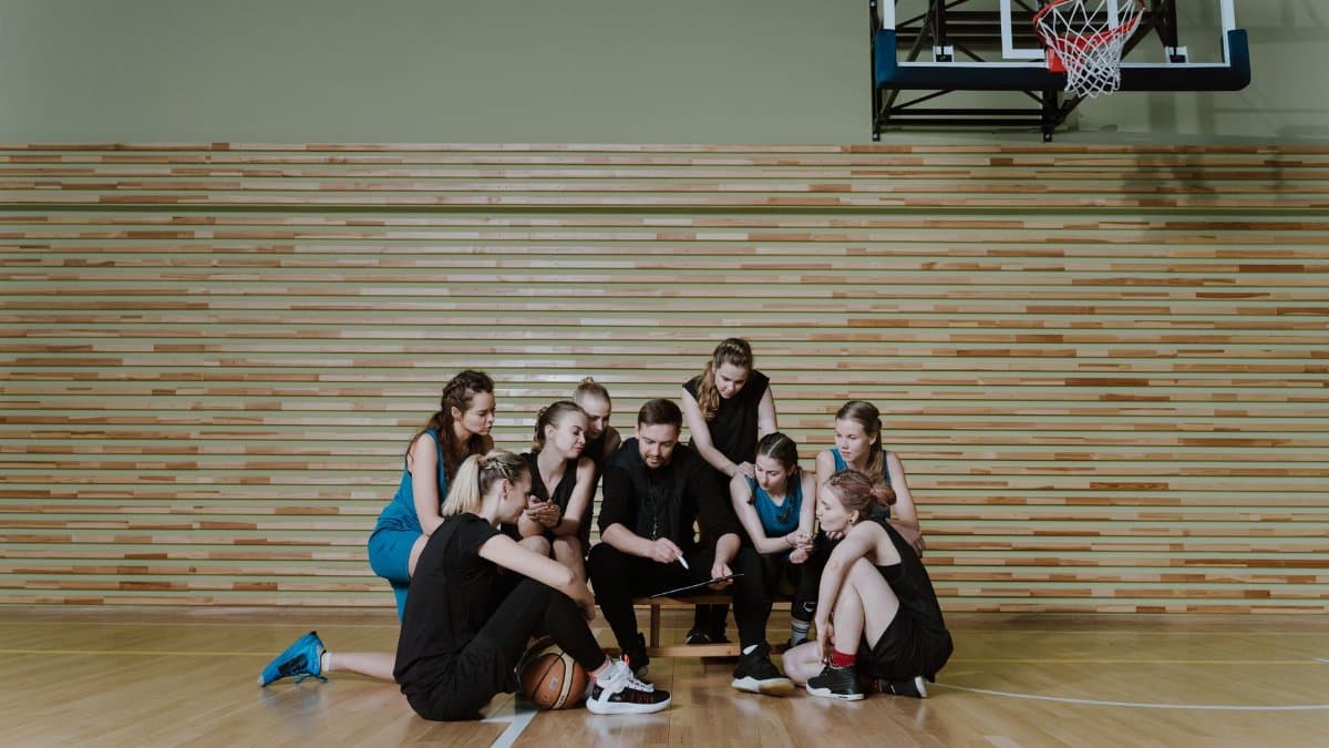 A coach discussing strategies with a female basketball team indoors on a court.