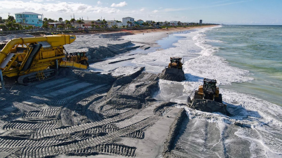 Beach restoration work with heavy machinery along a coastal area, involving sand dredging and bulldozers.