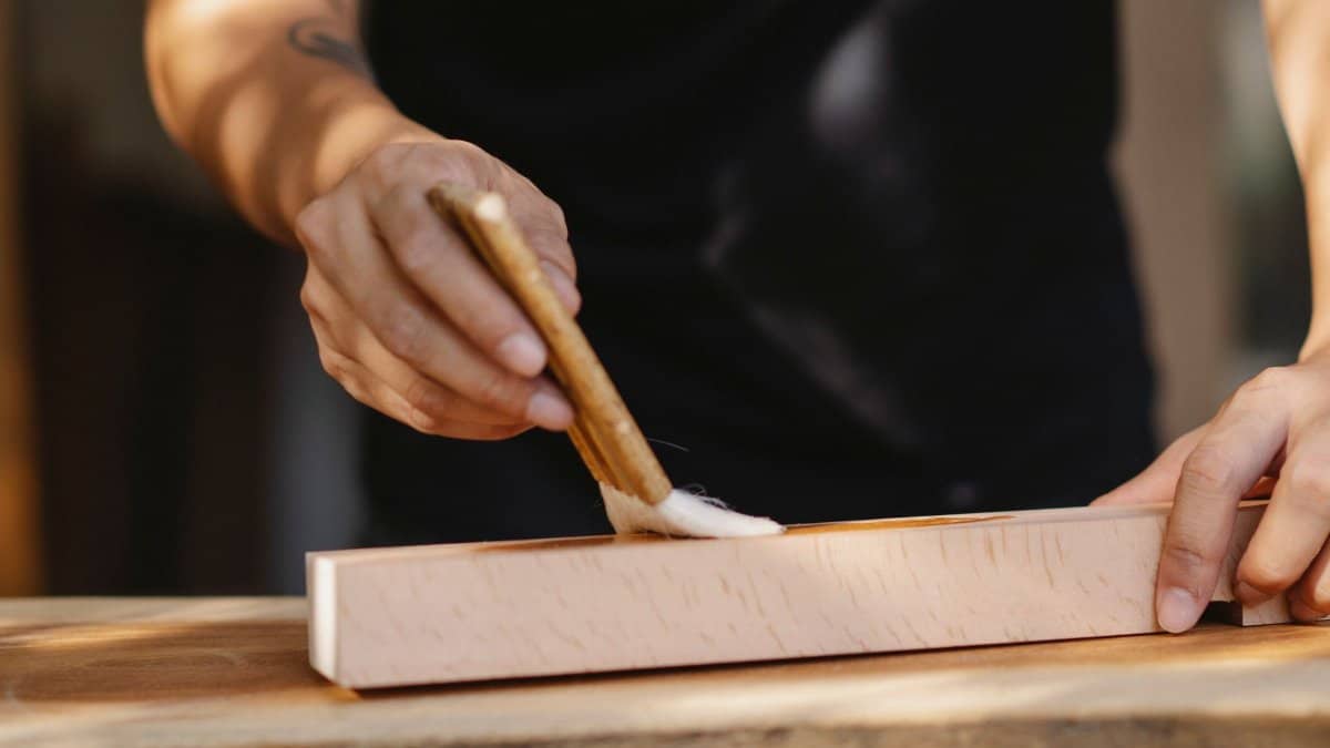Crop unrecognizable joiner washing wooden beam with varnish while creating handicraft in workshop