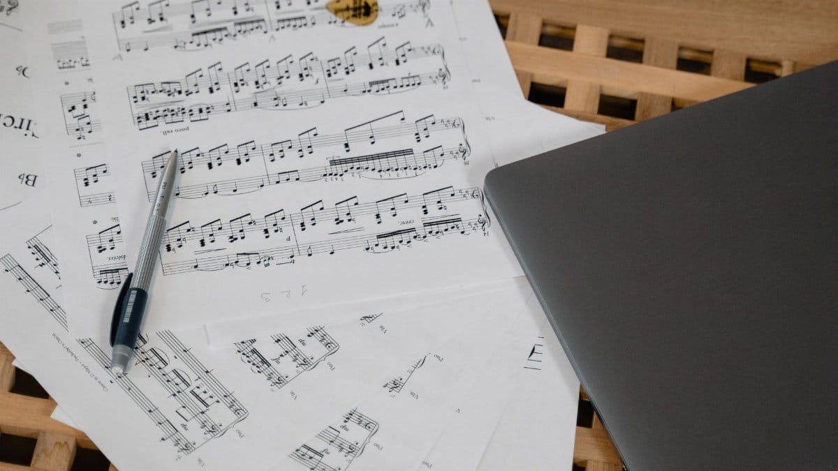 Close-up shot of music composition with laptop and guitar pick on a wooden table.