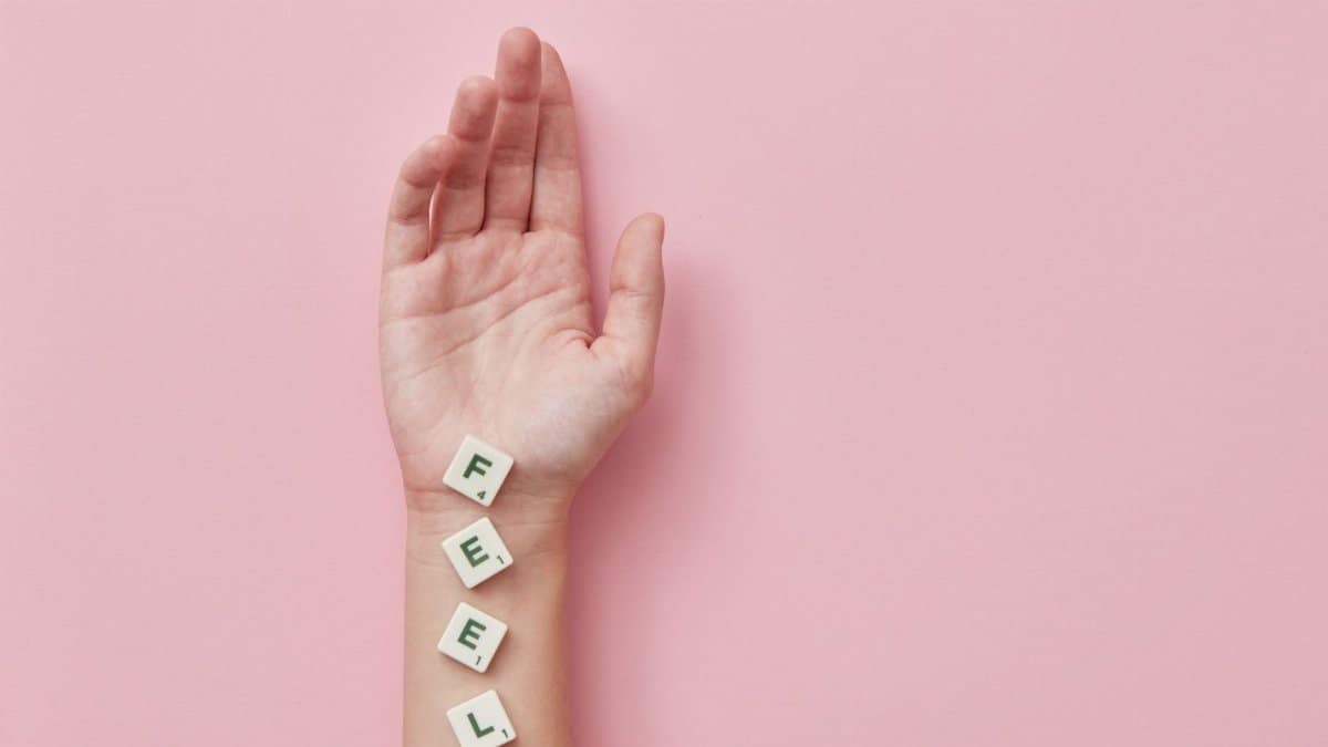 A minimalist photograph of a hand laid on pink background spelling 'FEEL' with Scrabble tiles.