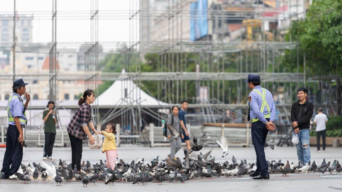 People feeding pigeons in a bustling public square in Ho Chi Minh City, Vietnam.