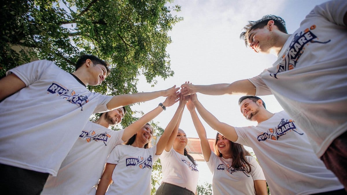 A group of young adults in white shirts sharing a joyful team moment outdoors.