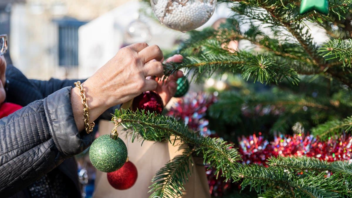 A person decorates an outdoor Christmas tree with colorful ornaments, creating a festive holiday atmosphere.