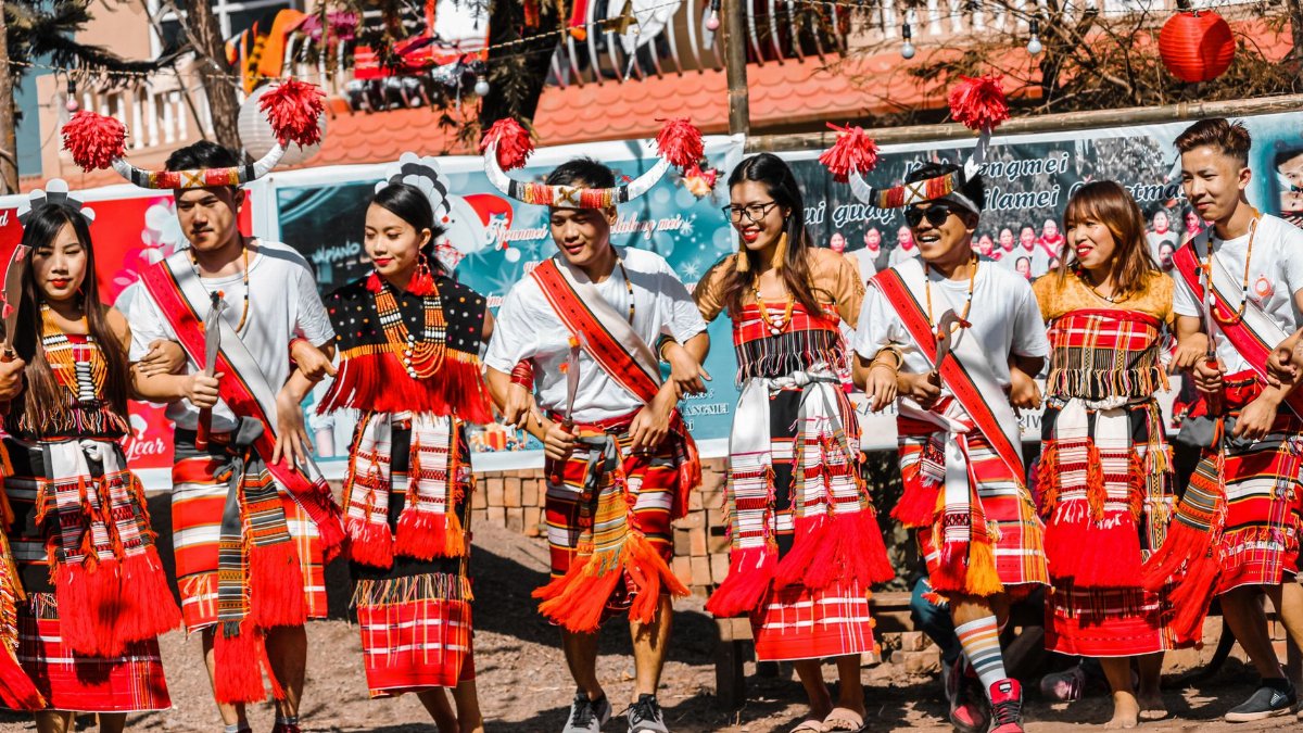 A group of people performing a traditional cultural dance outdoors, wearing tribal costumes.
