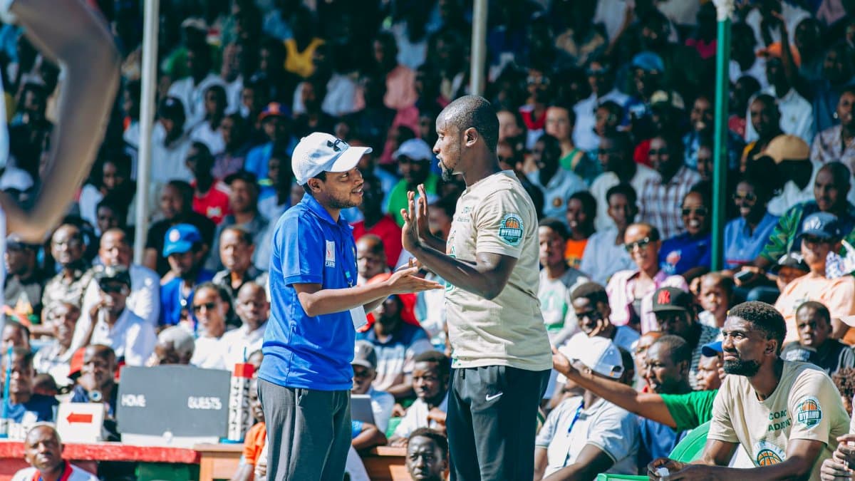 Lively outdoor basketball game scene with two coaches conversing, engaging audience in the background.
