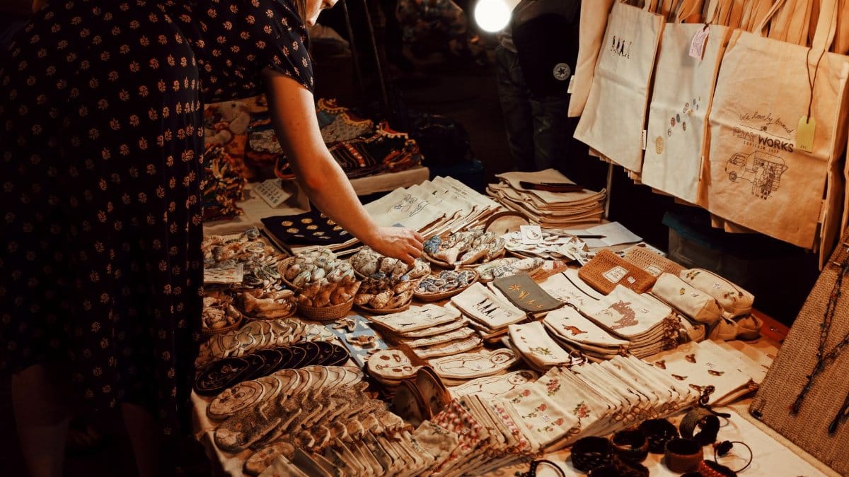 From above crop female customer in dress choosing handmade goods from table in local souvenir bazaar in evening