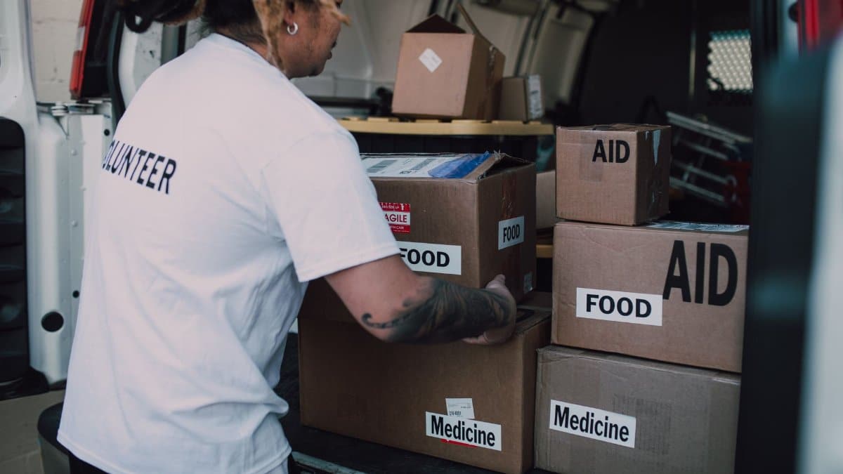 A volunteer organizes aid boxes containing food and medicine in a van for community service.